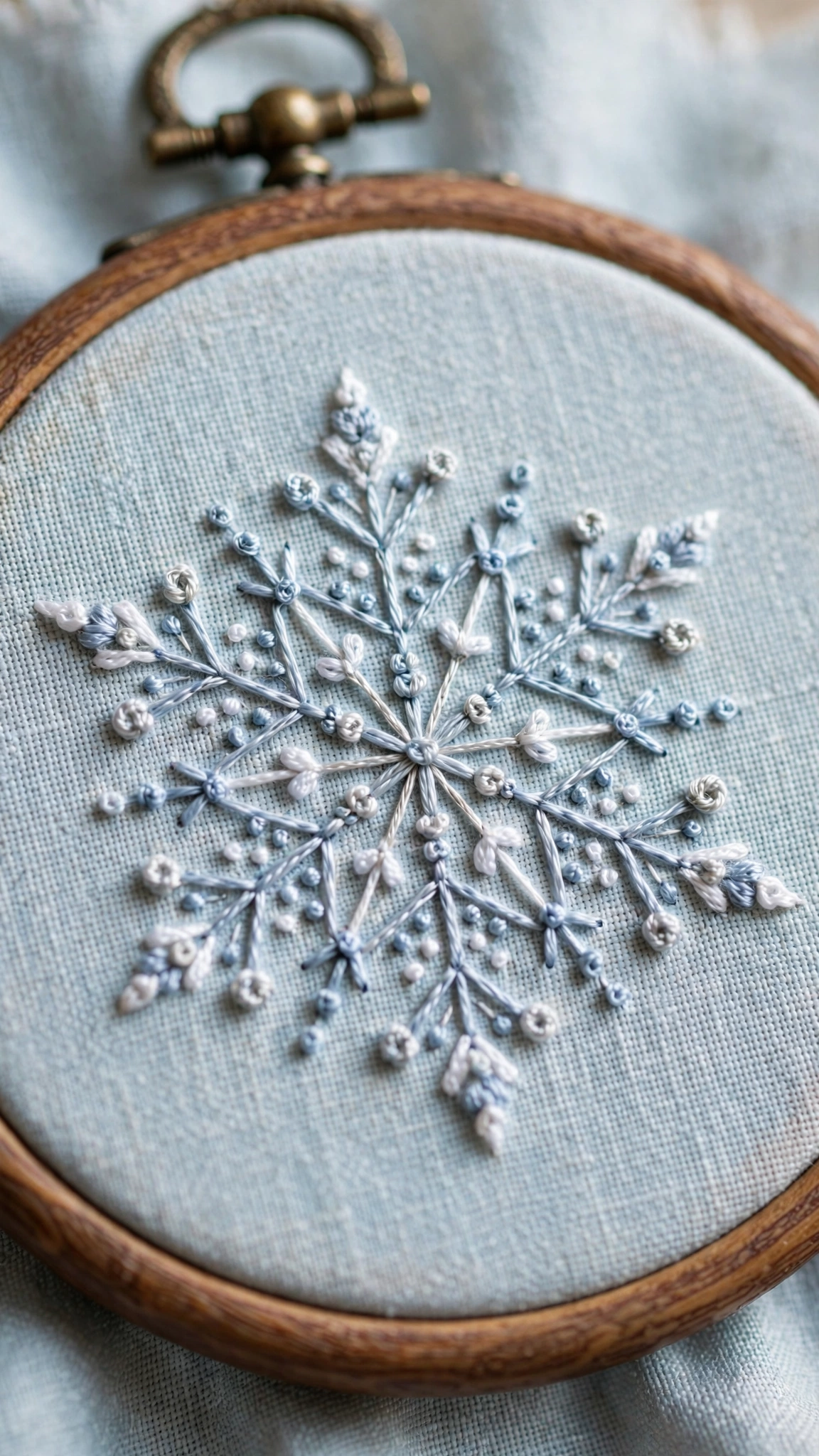 Delicate hand embroidered snowflake in silver blue and white floss with French knot details on pale blue linen