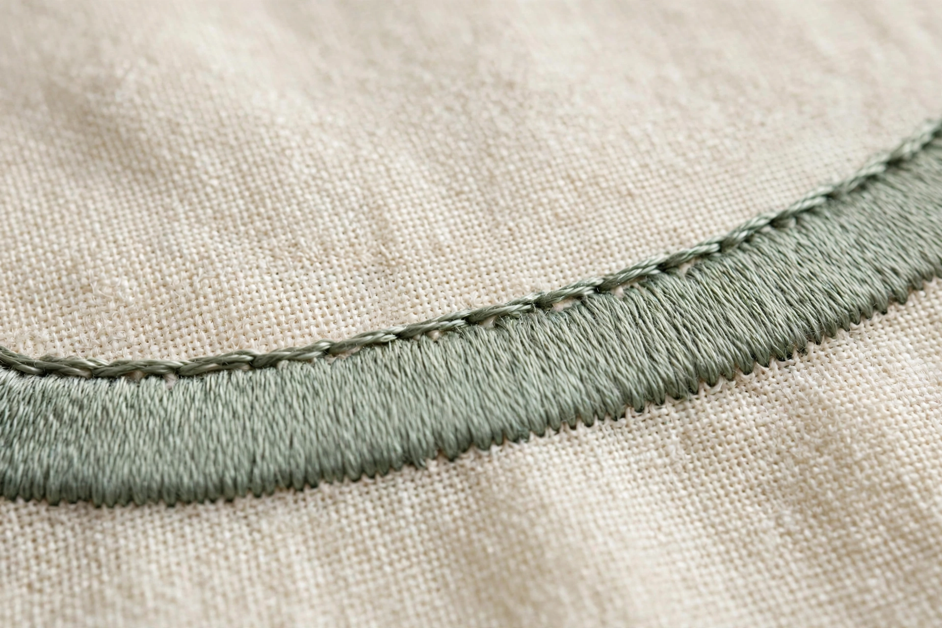 Close-up of hands stitching a satin stitch padding layer of split stitches under a petal outline on linen, process shot