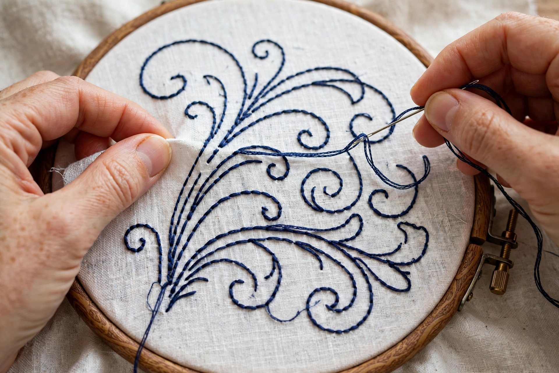 Close-up of a hand tracing printed lettering onto fabric with a blue water-soluble pen, pattern paper beneath, bright dayligh