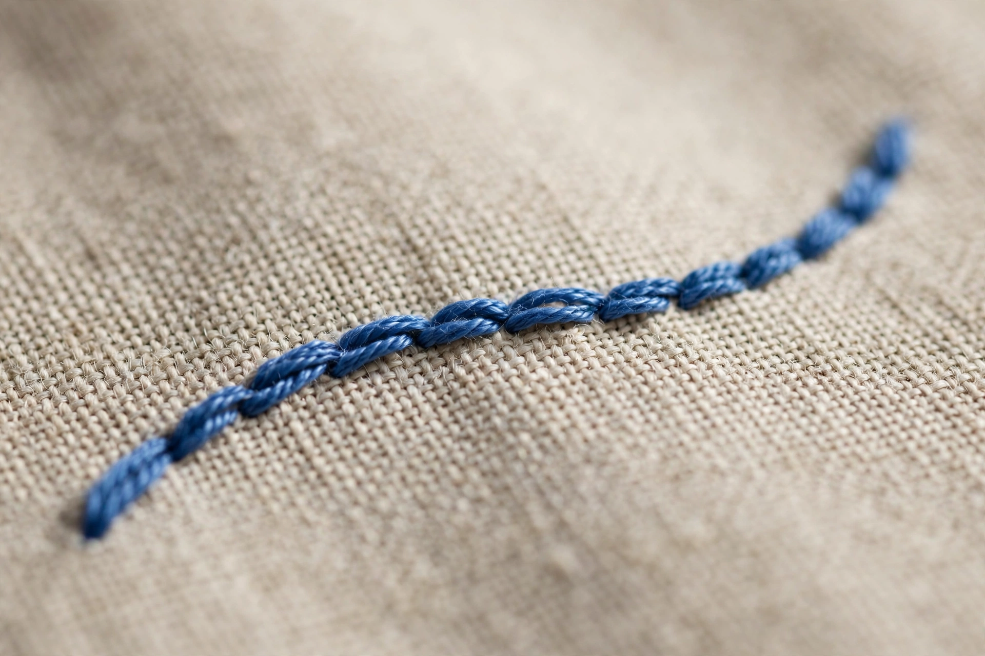 Photorealistic macro of short even stem stitches following a gentle curve in blue floss on linen, shallow depth of field, daylight, landscape orientation, no text