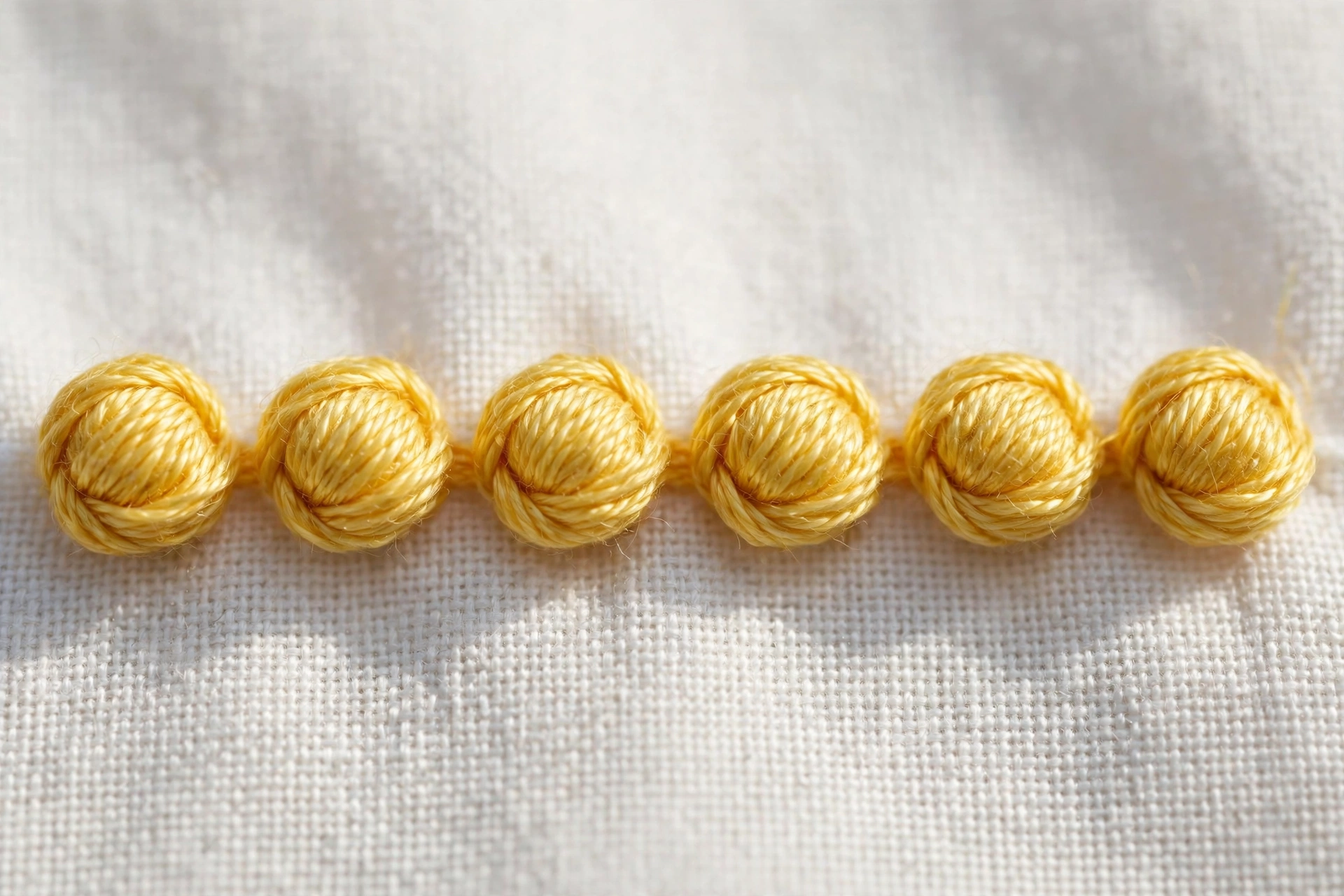 Photorealistic macro of a neat row of uniform round colonial knots in yellow floss on white fabric, daylight, landscape orientation, no text